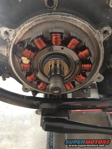 Motorcycle stator with copper windings and a splined rotor assembly. Part of the engine casing and frame are visible