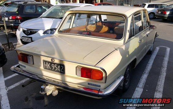 Rear view of a beige sedan parked in a lot. Another car is visible behind it