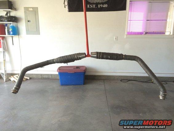 Two black motorcycle exhaust pipes with heat wrap, suspended by a red pole