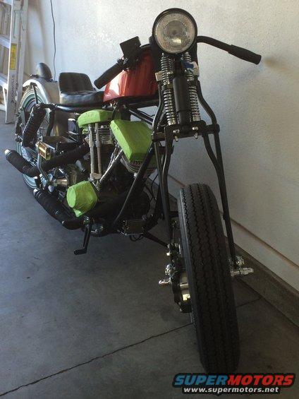 Chopper motorcycle with green engine covers and a red gas tank, viewed from the front three-quarter angle