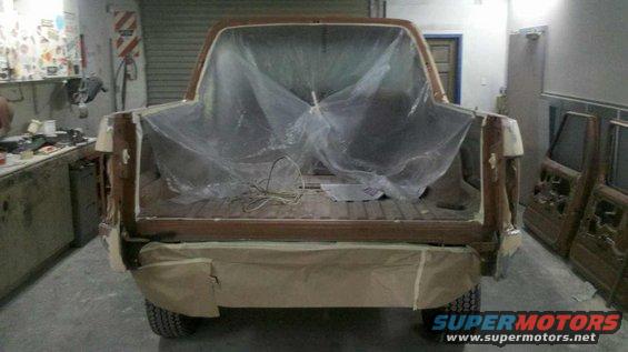 Rear view of a brown 1980s Ford Bronco undergoing bodywork, covered in plastic sheeting