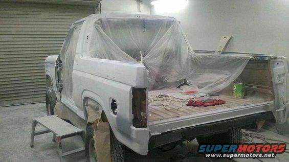 Ford Bronco with doors removed, covered in primer and plastic sheeting, in a workshop