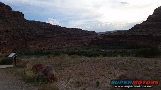 Desert canyon landscape with a river and vegetation, under a cloudy sky