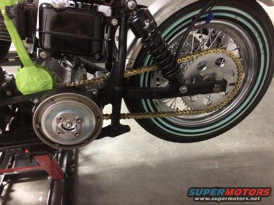 Motorcycle rear wheel, gold chain, and black shock absorber. Tire has light blue stripes