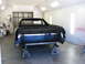 1973 Ford Ranchero - The rear of a black 1972 Ford Ranchero is visible, supported by jack stands inside a paint booth.