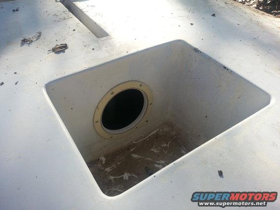 Close-up of a white boat deck with a square opening revealing a circular hatch