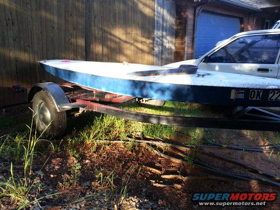 Boat on a trailer with a car visible behind it. License plate reads '2001 OK 22'