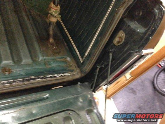 Green interior of a 1978 Ford Bronco with visible rust and dirt around the tailgate hinges