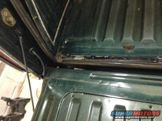 Interior view of a dark green vehicle's cargo area, showing ribbed metal and hinges