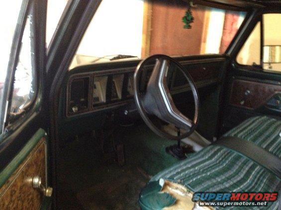 Green striped seat with torn upholstery, dark dashboard with rectangular gauges, and a two-spoke steering wheel