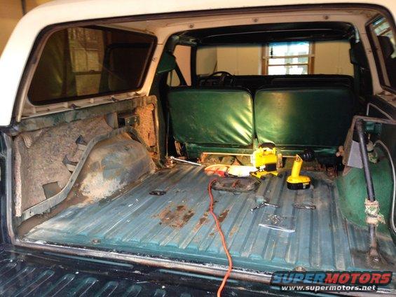 Back of SUV with green seats, tools on floor, and some rust