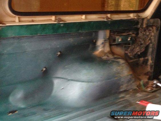 Rear cargo area of a vehicle, showing green painted metal floor and wheel well. Some rust and debris visible