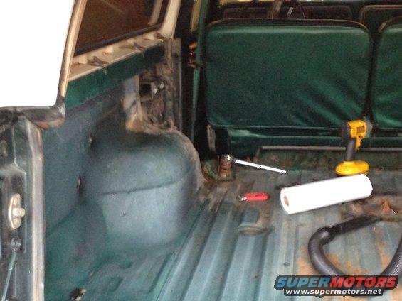 Green interior of a 1978 Ford Bronco with a roll of paper towels, a drill, and a vacuum hose