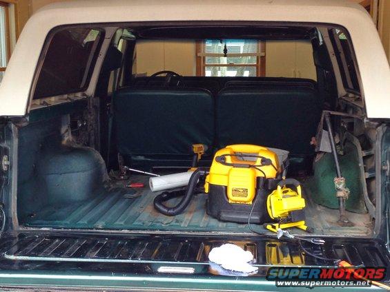Interior of a 1979 Ford Bronco with a shop vac and other cleaning tools in the cargo area