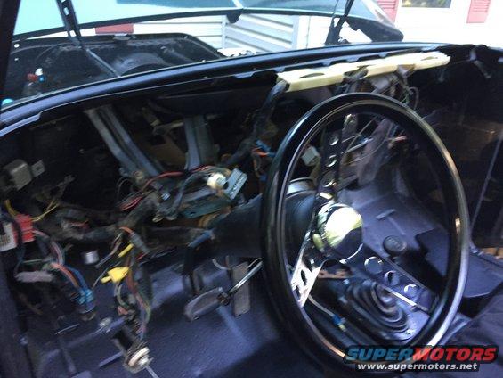 Car interior with dashboard removed, showing wiring harness and steering column