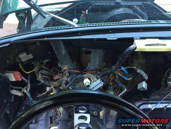 View of a vehicle's dashboard with the wiring harness exposed. Steering wheel is visible in the foreground