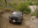 1988 Ford Bronco - Black SUV with a winch on the front bumper navigates a dirt road with surrounding vegetation.
