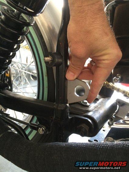 Hand holding a metal bracket against a motorcycle frame near the rear shock and chain