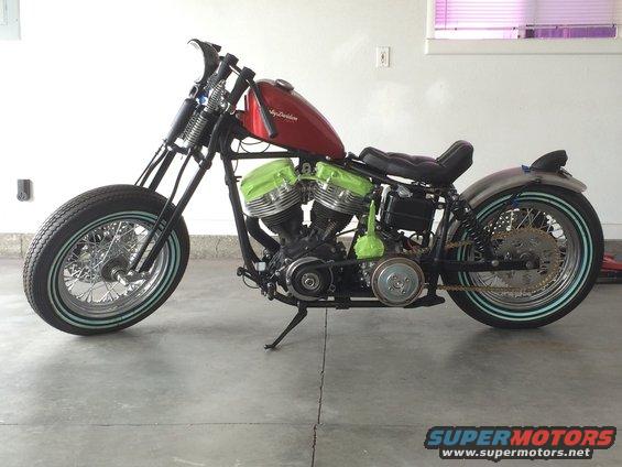 Custom motorcycle with red fuel tank and green engine covers, parked indoors