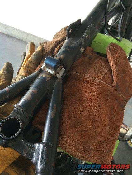 Close-up of a motorcycle frame section with welding. Hands in gloves are holding it