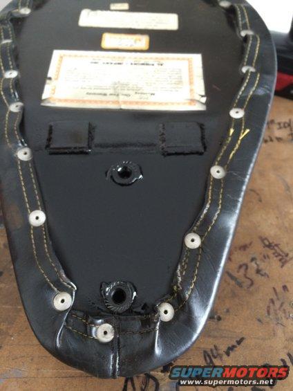 Underside of a black motorcycle seat with yellow stitching and two labels