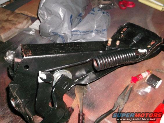 Black metal car part with a coiled spring and pliers nearby