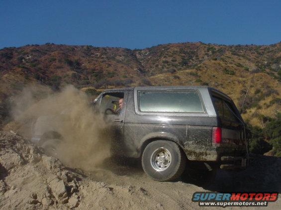 Ford Bronco kicking up dust on a dirt trail with hills in background