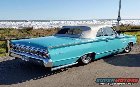 Blue convertible with a tan top parked by the ocean. Rear view