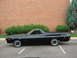 1973 Ford Ranchero - A black 1972 Ford Ranchero is parked in a lot with a brick building and bushes in the background.