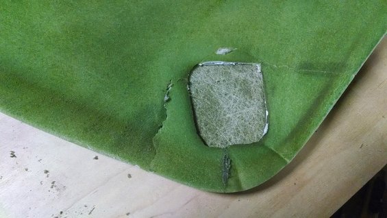 Green automotive headliner material with a rectangular cutout revealing fibrous backing