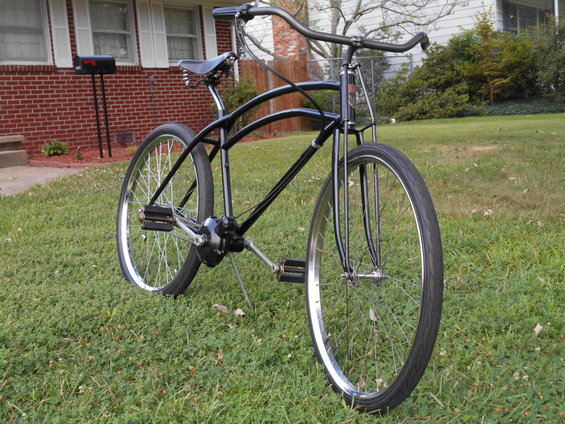 black cruiser bicycle with curved frame and chrome rims parked on grass in front of a brick house