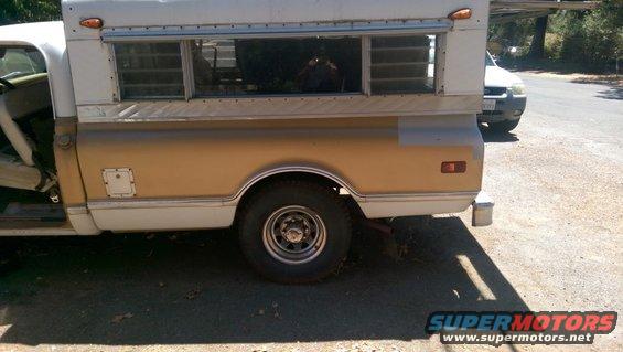 Pickup truck side view, gold and white camper shell, visible interior, another vehicle behind