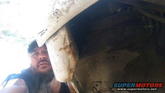 Man peers into a rusted wheel well of a vehicle