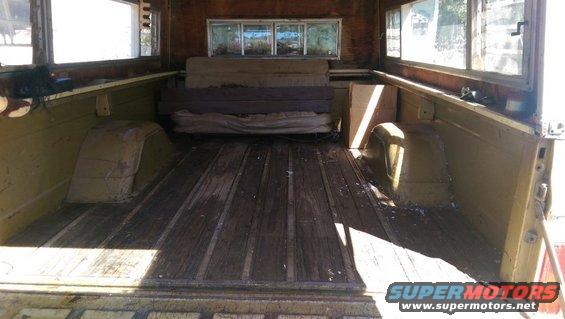 Interior of a pickup truck bed with wooden floor and side panels, showing wheel wells and stacked items