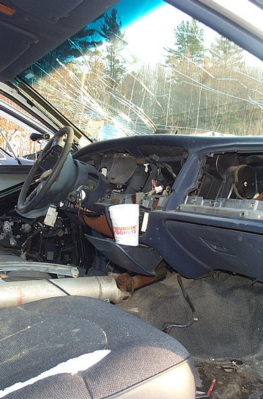 Interior of a car with a cracked windshield, missing dashboard parts, and a Dunkin' Donuts cup