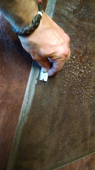 Hand holding razor blade scraping residue from glass edge