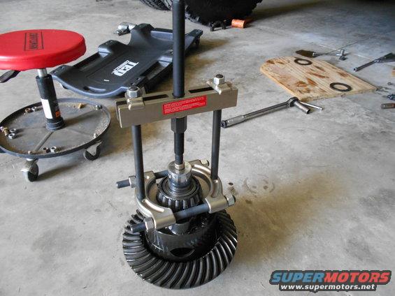 differential gear with bearing puller tool attached, red creeper seat, and socket wrench on concrete floor
