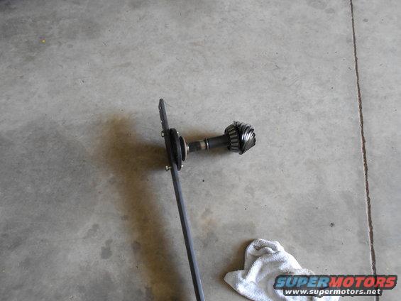 Differential gear assembly with a metal rod attached, lying on a concrete floor next to a white cloth