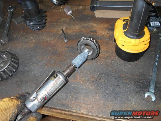 Grinding a bearing race with a rotary tool on a workbench with gears and wrenches