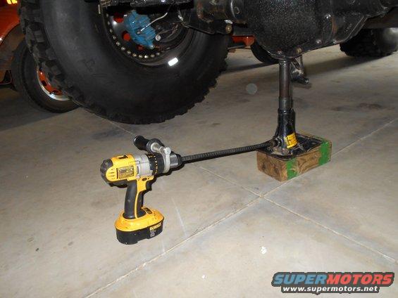 Power drill attached to a jack screw, lifting a vehicle's rear axle