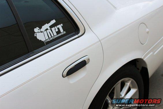 White sedan's rear passenger door and window, showing a chrome door handle and a white performance sticker