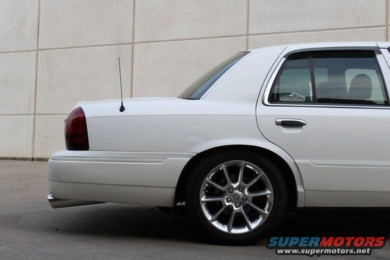 White sedan's rear quarter panel and wheel. Has a sticker on the rear window