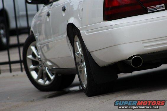 Rear quarter panel and wheel of a white sedan. Has a SuperMotors watermark