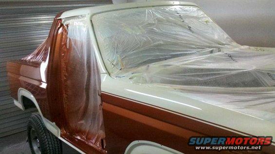 side view of a truck covered in plastic sheeting, with some parts exposed for painting