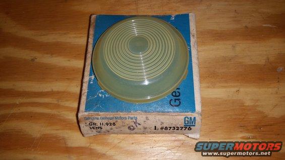 Yellowish-green ribbed lens in a blue and white General Motors parts box on a wooden surface