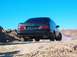 1990 Ford Taurus - Rear view of a black 1990 Ford Taurus parked on a dirt road with a clear blue sky overhead.