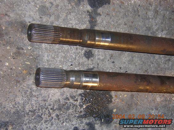 Two rusty axle shafts with splined ends resting on a concrete surface