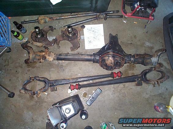 Disassembled Dana 44 front axle components, including knuckles, hubs, and differential housing, laid out on a concrete floor