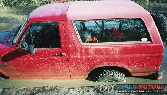 Red Ford Bronco stuck in mud, side view. Visible Metallica sticker on rear window