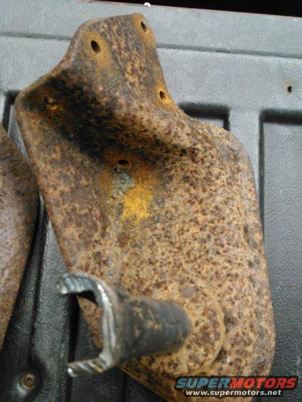 Rusty metal bracket with a bolt attached, resting on a dark surface